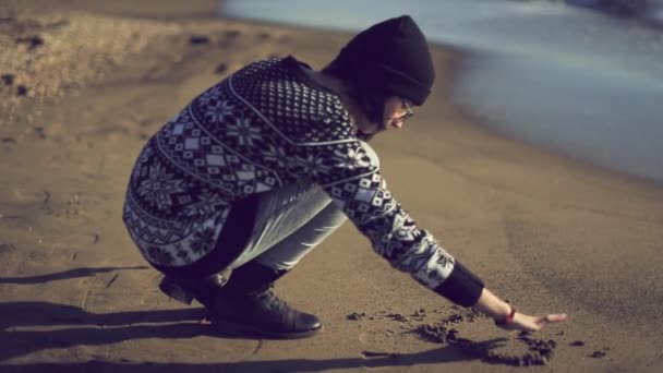 Девушка, рисующая сердце на песке — стоковое видео