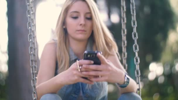 Lány a swing és smartphone — Stock videók