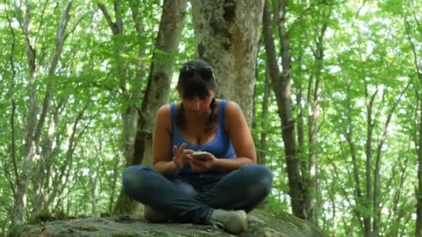 Mujer sentada en una roca usando un smartphone — Vídeo de stock