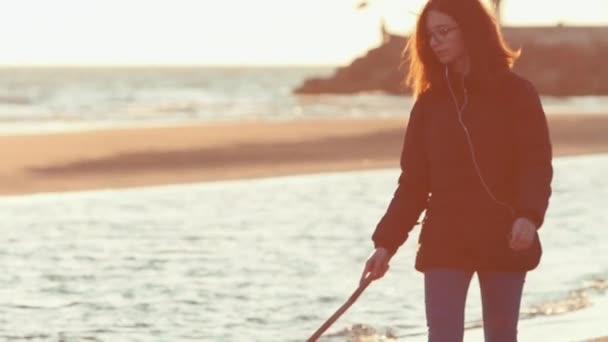 Ragazza sulla spiaggia che disegna sulla sabbia con un bastone. Girato al rallentatore — Video Stock