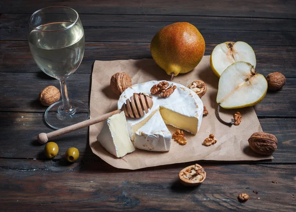 Сир камамбер з волоськими горіхами, медом і грушами на сільському столі. Склянка білого вина — стокове фото