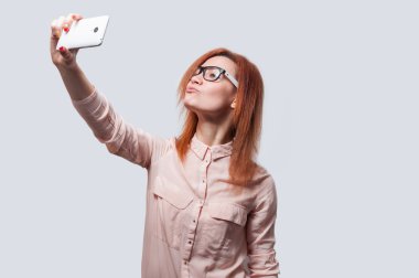 Gri bir arka planda izole edilmiş akıllı telefondan selfie çeken çekici bir kadının portresi.