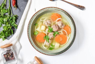 Köfte çorbası ve malzemeler beyaz ahşap masada..