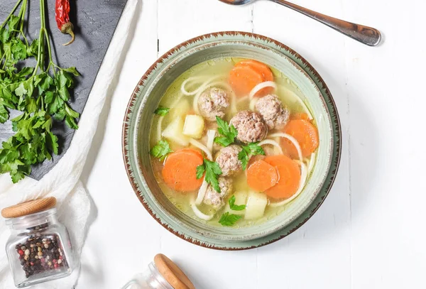 Köfte çorbası ve malzemeler beyaz ahşap masada..