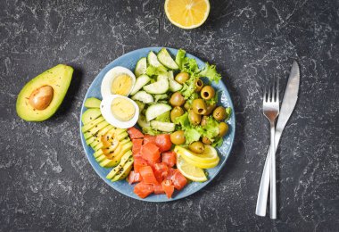 Ketogenik, paleo diyet kasesi tuzlanmış somon balığı, limon, avokado, zeytin, haşlanmış yumurta, salatalık, yeşil marul salatası, sağlıklı beslenme eğilimi, üst görünüm.