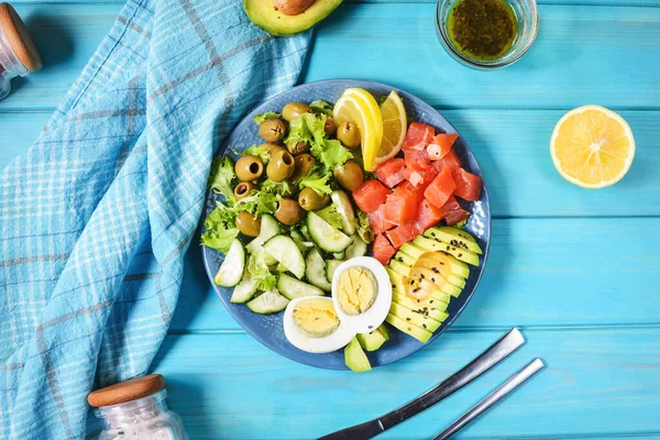 Кетогенна, палеодієтична страва з солоною рибою лосося, лимоном, авокадо, маслинами, вареним яйцем, огірком, зеленим салатом салатом салату, здоровою харчовою тенденцією, зверху. — стокове фото