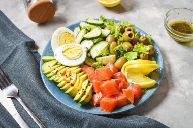 Ketogenik, paleo diyet kasesi tuzlanmış somon balığı, limon, avokado, zeytin, haşlanmış yumurta, salatalık, yeşil marul salatası, sağlıklı beslenme eğilimi.