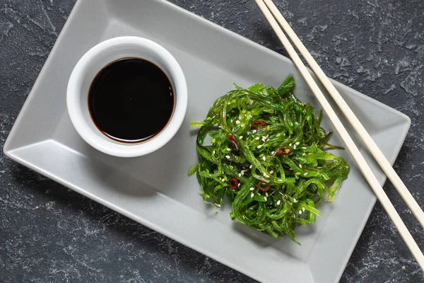 Wakame seaweed salad with sesame seeds and chili pepper in a bowl on black stone background. Top view — Stock Photo, Image