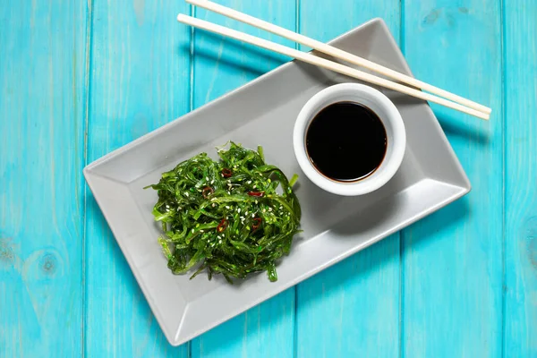 Wakame seaweed salad with sesame seeds and chili pepper in a bowl on blue wooden background. Top view — Stock Photo, Image