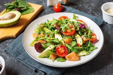 Salmon salad with green leaves, avocado and cherry tomato on stone background.