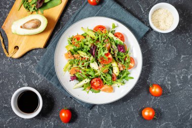 Yeşil yapraklı somon salatası, avokado ve siyah taş arka planda vişneli domates. Üst görünüm