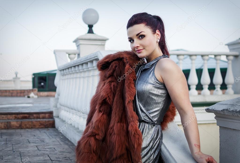 fashion outdoor photo of sexy glamour woman with dark hair wearing luxurious fur coat and leather gloves