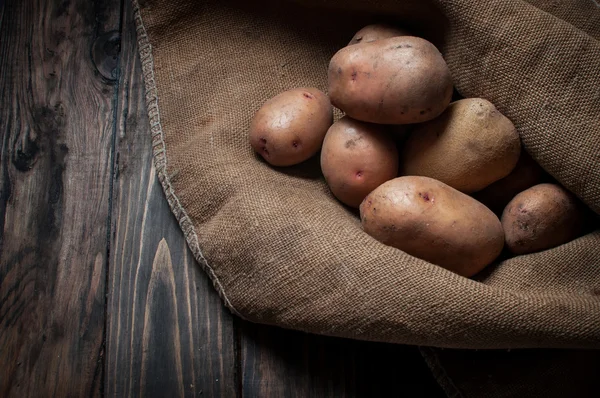 Harvest potatoes in burlap sack on wood background. — Stock Photo, Image