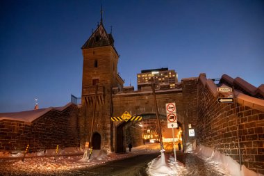 Geceleri karla kaplı cadde ile tarihi şehir kapısı manzarası. Quebec Şehri, Kanada - 21 Aralık 2025.