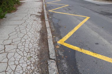 Sarı zigzag yolu işaretli ve hasar görmüş asfalt dokusu altyapıyı ve şehir bakımını sembolize ediyor..