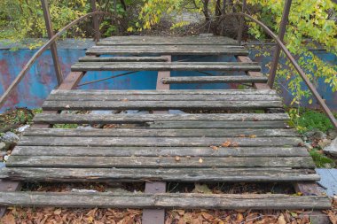 Sonbahar yaprakları ve bitki örtüsüyle çevrili eski terk edilmiş ahşap köprüler ve paslı metal korkuluklar..