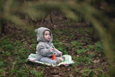 Küçük çocuk parkta açık bir çayırda oturuyor. Akşam ormanındaki ve mahalledeki çocuk yukarı bakıyor..