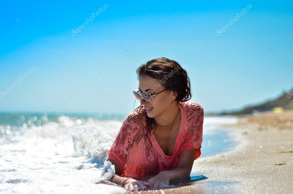 Beautiful smiling girl lie on the beach under the sun washed by foaming waves
