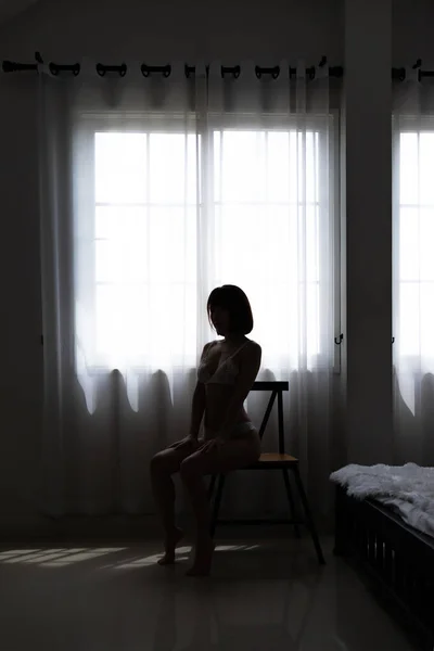 Silhouette asian young woman wearing sexy bikini and sitting on chair in bedroom.