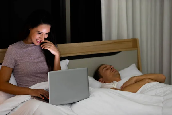 Женщина Сидящая Кровати Ночью Используя Ноутбук Пока Муж Спит Рядом — стоковое фото