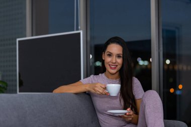 Gecenin bir yarısı bir fincan çayın keyfini çıkaran bir kadın evdeki oturma odasında bir kanepede oturuyor.