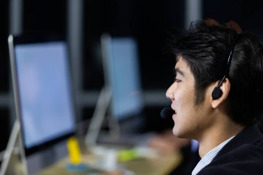 Kulaklık takan bir iş adamı iş arkadaşlarıyla birlikte gece geç saatlere kadar çağrı merkezinde çalışıyor. Gece iş konsepti.