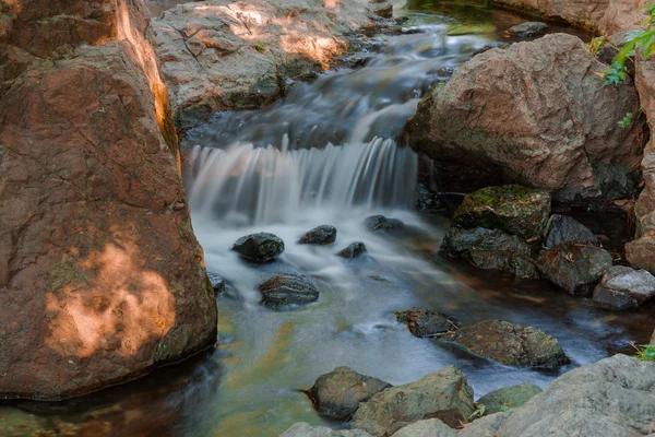 Water falls over a jumble of moss-covered boulders in forest. — Stock Photo, Image