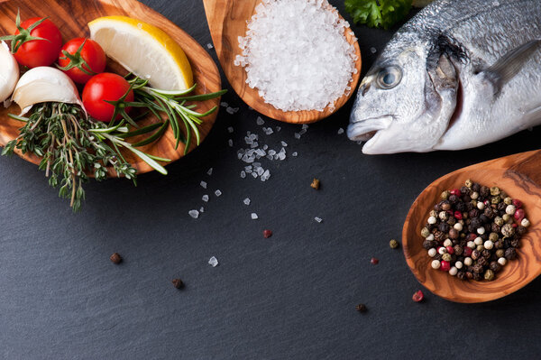 fresh  raw  dorado  fish  with  spices  and herbs on black background, top view