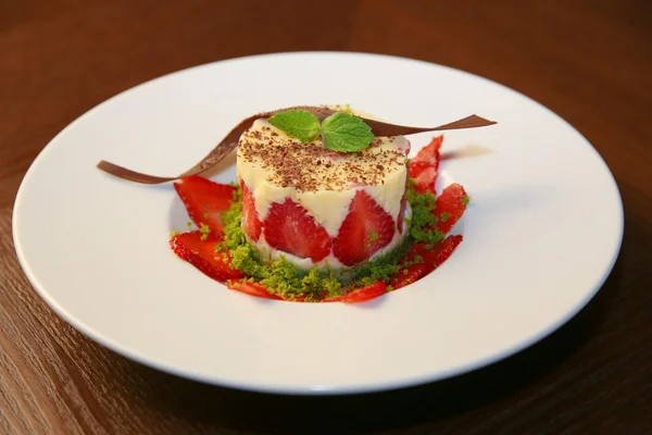 Layered dessert with strawberries, biscuit cake and cream cheese on a dark wood background — Stock Photo, Image