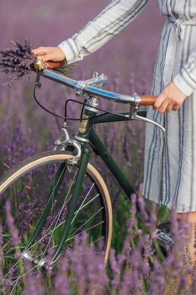 Νεαρή γυναίκα με ρετρό ποδήλατο και μπουκέτο λεβάντας σε βιολετί φόντο τομέα λουλούδια — Φωτογραφία Αρχείου