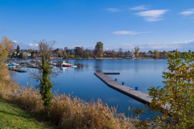 Rıhtımlı ve tekneli sakin bir göl manzarası, muhtemelen dinlenmek için. Sakin su ve berrak gökyüzü tekneyle gezmek ve rıhtımın tadını çıkarmak için huzurlu bir gün olduğunu gösteriyor..
