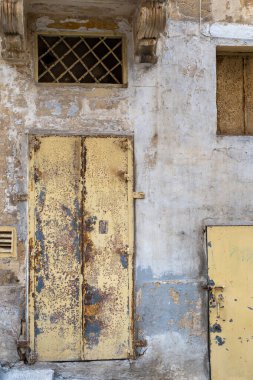 Zaman etkisini gösteriyor: eski bir bina üzerindeki yıpranmış sarı kapılar ve soyulmuş boyalar yaşın ve ihmalin etkilerini gösteriyor, dokulu, kırsal bir sahne yaratıyor..