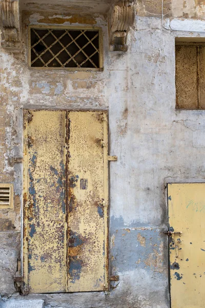 Zaman etkisini gösteriyor: eski bir bina üzerindeki yıpranmış sarı kapılar ve soyulmuş boyalar yaşın ve ihmalin etkilerini gösteriyor, dokulu, kırsal bir sahne yaratıyor..