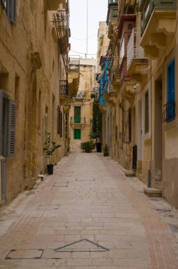 Malta, Valletta 'da tarihi binalarla dolu dar, tuğlalı bir cadde. Mimari renkli balkonlar ve panjurlar sergiliyor, büyüleyici, eski dünya atmosferi yaratıyor..