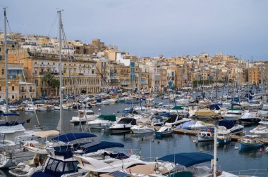 Malta 'da tekneler ve yatlarla dolu hareketli bir liman sahnesi. Şehrin tarihi mimarisi arka planda yükselir ve güzel bir manzara yaratır..