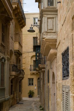 Malta, Valletta 'da dar bir sokakta şehrin eşsiz mimarisi sergileniyor. Yerel kireçtaşından inşa edilen binalar, kapalı ahşap balkonlar ve karmaşık demir işçiliği içeriyor..