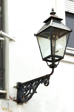 Süslü, eski bir gaz lambası beyaz bir duvara monte edilir. Muhtemelen binanın estetik cazibesini artırmak ve aydınlatmak için..