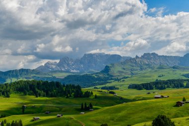 Dolomitlerin manzarası, İtalya. Bereketli yeşil çayırlar ve ahşap kulübeler manzarayı doldurarak turistler için huzur verici bir dağ manzarası yaratıyor..