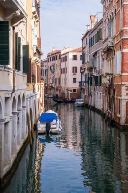 Venedik, İtalya 'da yolcu taşıyan bir gondolcu. Kanal boyunca renkli binaları yansıtan tekneler yanaştı..