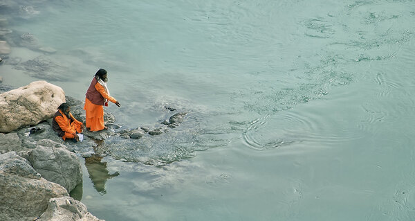 Rishikesh, India - March 10, 2014: Indian men fed the fish in the  Ganges