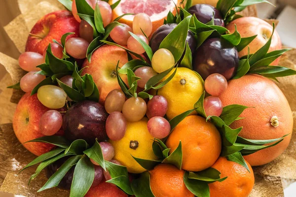 Fruit bouquet of apples, lemons, plums, grapes, tangerines, grapefruit and green leaves close up