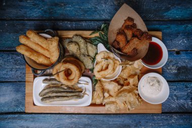 Yukarıdan mavi arkaplan manzaralı ahşap tepside biraya atıştırmalıklar.