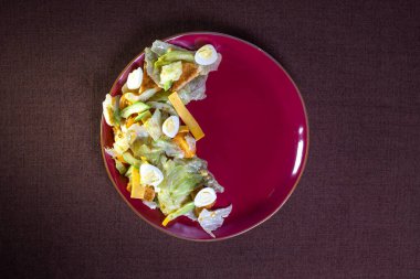 Yumurtalı salata, peynir ve otlar bordo bir tabakta..