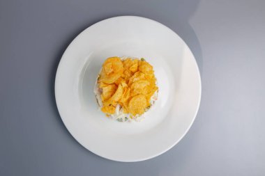 Tavuklu salata, salatalık ve cipsler beyaz tabakta..