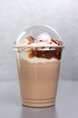 Gri arka planda plastik bardakta tatlı milkshake.