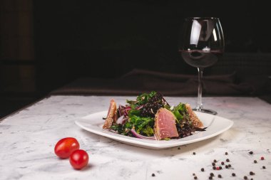 Balık salatası ve şaraplı beyaz tabakta otlar..