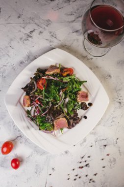 Beyaz tabakta balık ve otlu salata ve şarap..