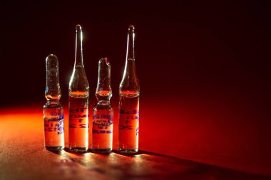 Kırmızı zemin üzerinde enjeksiyon ilacı bulunan dört şişe..