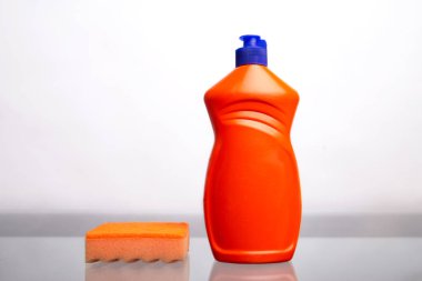 turuncu sünger ve beyaz arka planda temizlik maddesi olan şişe.
