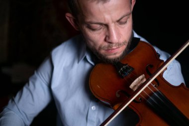 Bir adam siyah arka planda keman çalıyor..